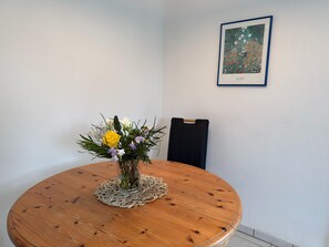 A round wooden table with a glass vase of flowers, a doily, and a chair. A framed artwork is on the wall. - Cozy Apartment in Zingst Germany Near Beach (Zingst)
