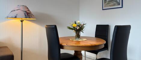 A dining area with a round wooden table, black upholstered chairs, a floor lamp, and a vase with flowers.
