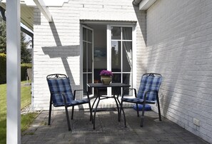 A patio with two blue plaid chairs and a table, a white brick wall, and a sliding glass door. - Cozy Apartment in Zingst Germany Near Beach (Zingst)