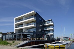 Un immeuble moderne à plusieurs étages, doté de balcons, d’une façade en verre et offrant une vue sur le front de mer.