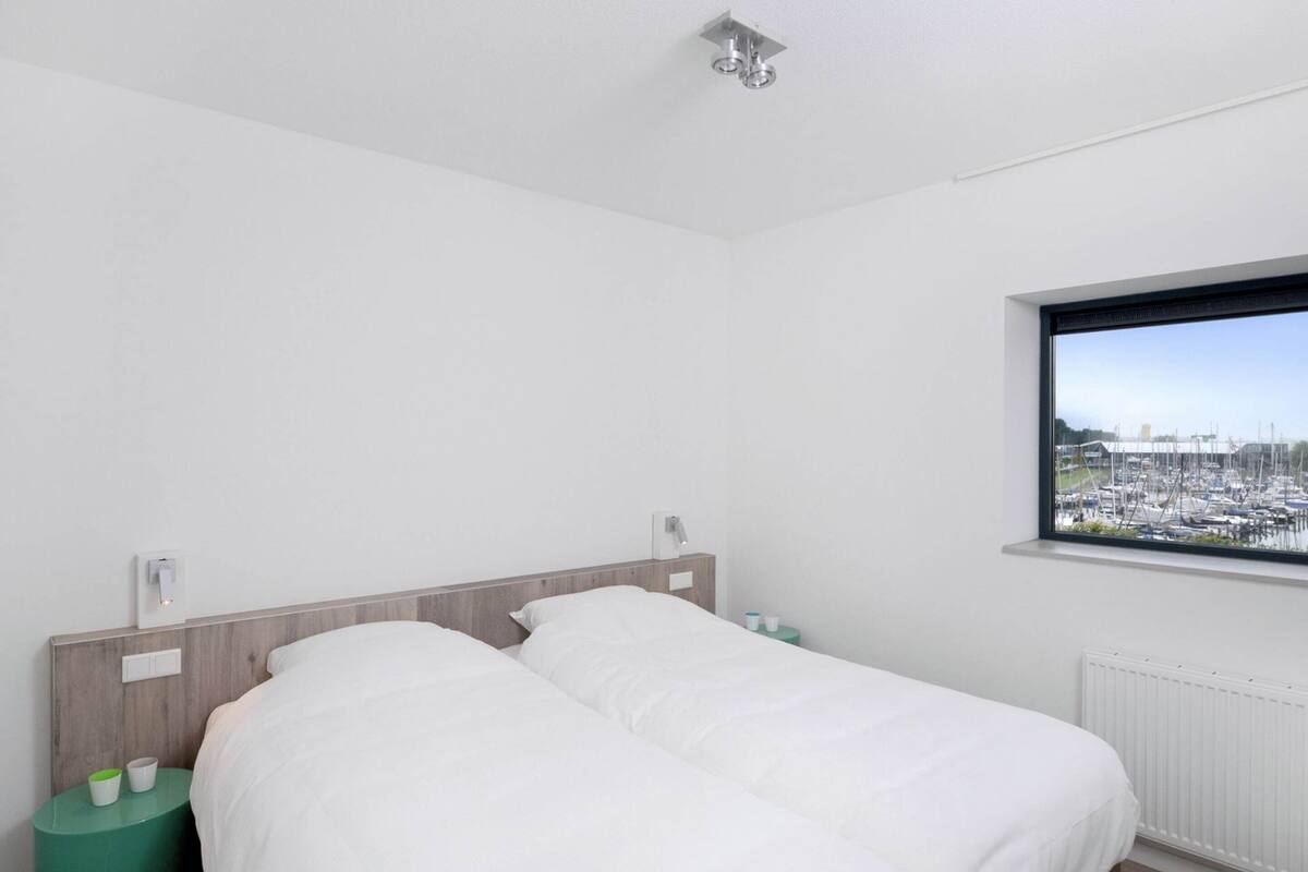 A bedroom with two beds, a view of a marina through a window, and a green side table with cups.