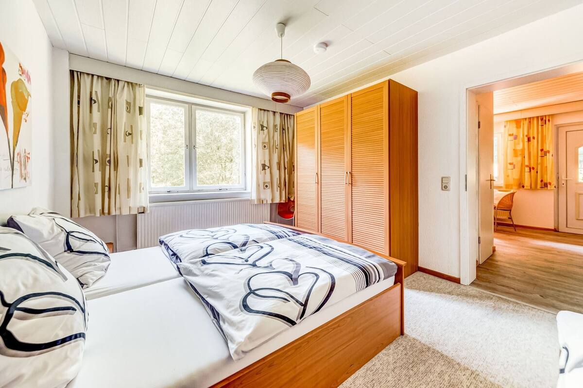 Ein Schlafzimmer mit Bett, Kleiderschrank, Fenster und einer Tür zu einem anderen Raum.