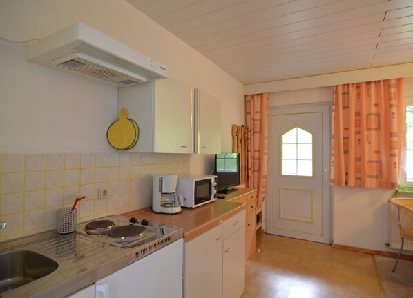 A kitchen with a stove, microwave, and coffee maker. There is a window with curtains and a door with a window.