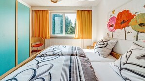 A bedroom with a bed, a chair, a window with curtains, and a wall with a floral painting. - Luxurious Apartment in Heubach Germany in the Forest (Masserberg)