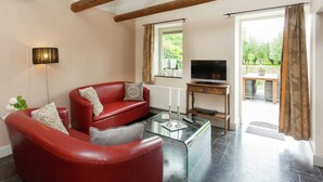 A living room with a red leather sofa, a glass coffee table, a TV on a wooden stand, and a window with curtains. - Stunning Holiday Home Near Forest in Slenaken (Slenaken)