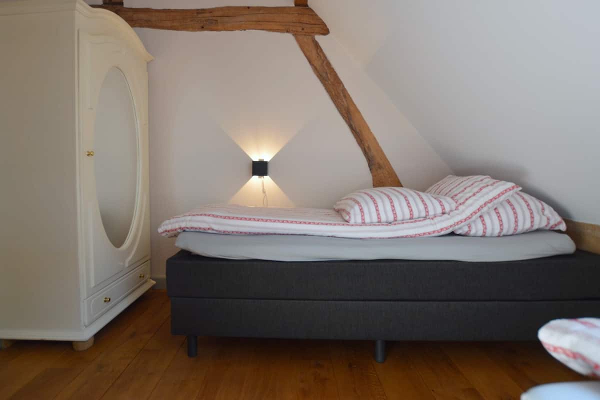 Une chambre à coucher avec un lit, une commode et une lampe fixée au mur.