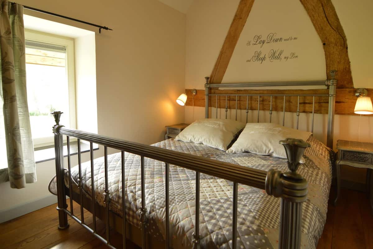 Une chambre à coucher avec un cadre de lit en bois, une tête de lit ornée d’un motif décoratif, deux lampes de chevet et une fenêtre avec des rideaux.