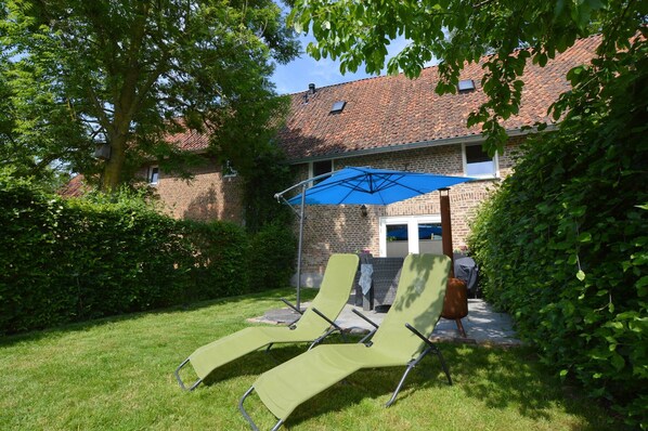 A backyard with a brick house, a blue umbrella, and two green lounge chairs. - Stunning Holiday Home Near Forest in Slenaken (Slenaken)