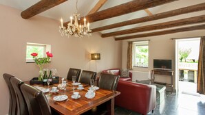A dining area with a wooden table set for six, surrounded by leather chairs. A chandelier hangs from the ceiling, and a red sofa is visible in the background. - Stunning Holiday Home Near Forest in Slenaken (Slenaken)