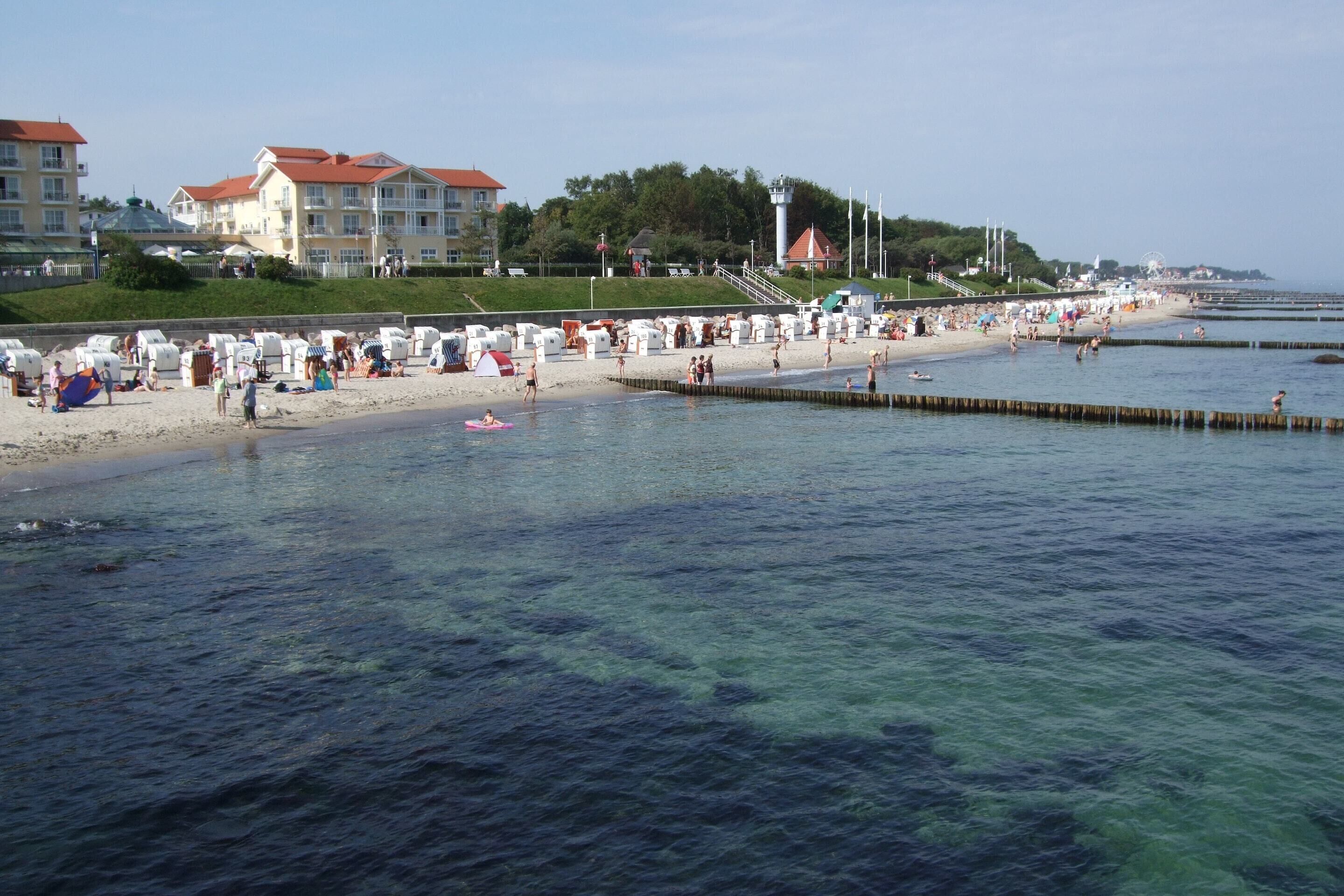 A beach with clear water, people, and buildings in the background.