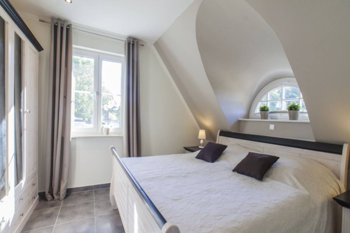 A bedroom with a large bed, a nightstand, a window with curtains, and a skylight.