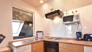 A compact kitchen with a dishwasher, oven, microwave, and a window with a view. - Snug Apartment in Kropelin Germany (Kroepelin)