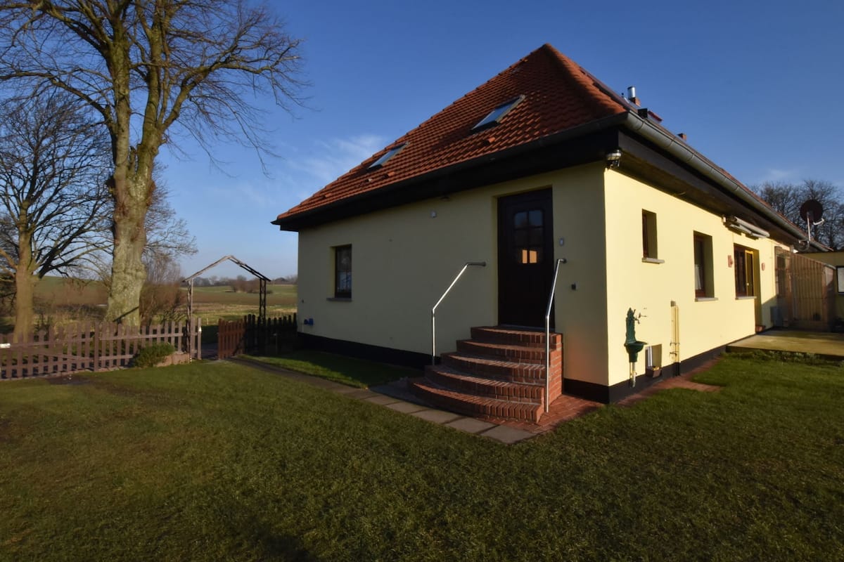 A single-story building with a red-tiled roof, a front door, and a small set of steps leading to the entrance.
