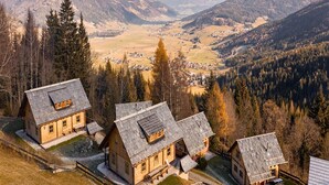 A cluster of wooden cabins with sloped roofs, surrounded by a forested landscape and distant mountains.
