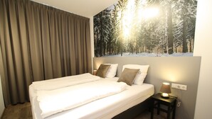 A neatly made bed with white linens and two pillows, a bedside table with a lamp, and a wall mural of a snowy forest scene.