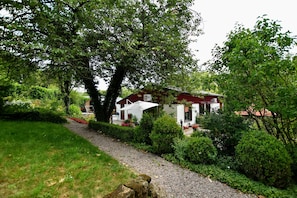 Ein Haus mit rotem Dach, umgeben von üppigem Grün und einem Kiesweg.