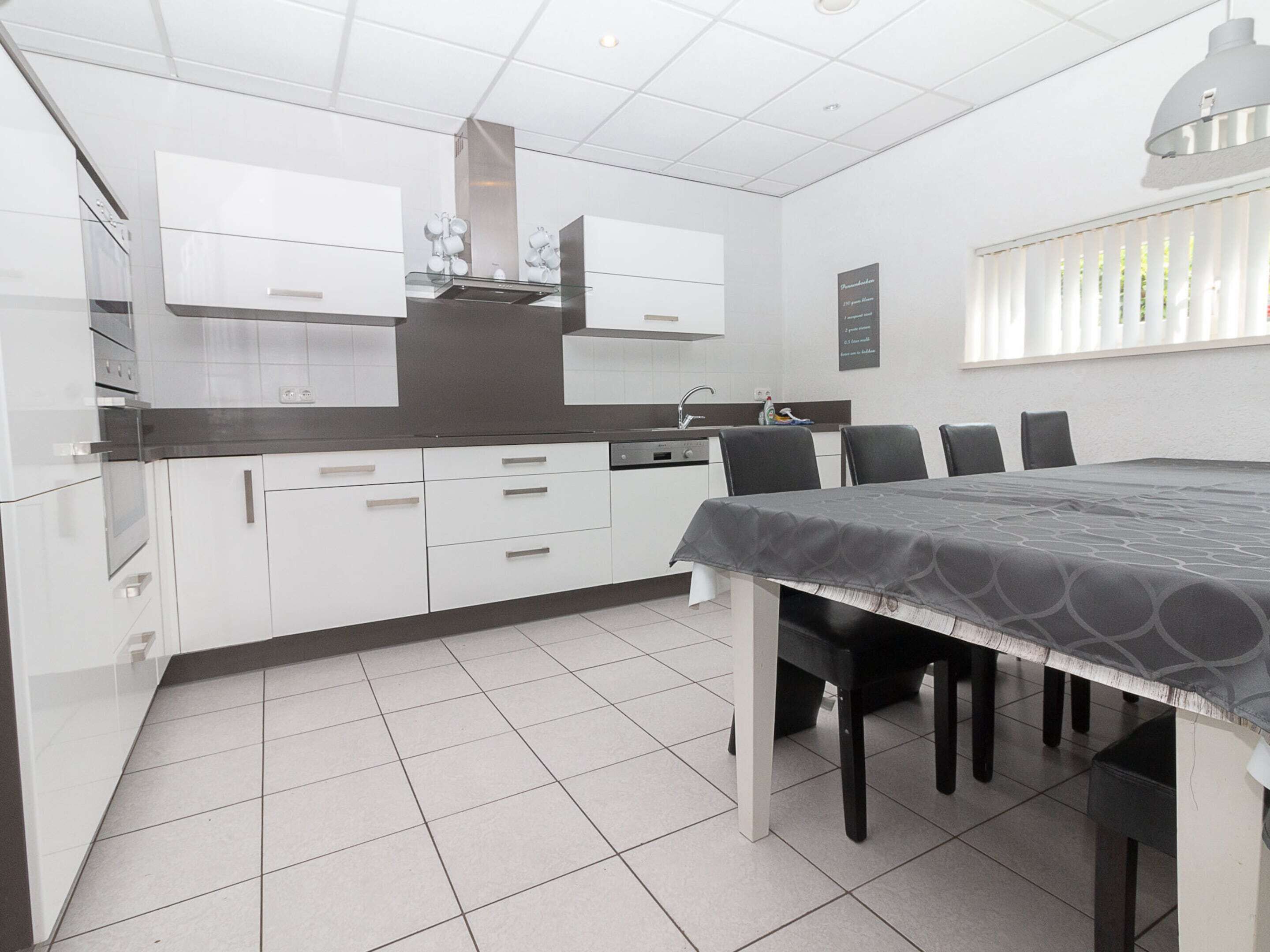 Una cocina moderna con armarios blancos, encimera negra y comedor con mesa y sillas.
