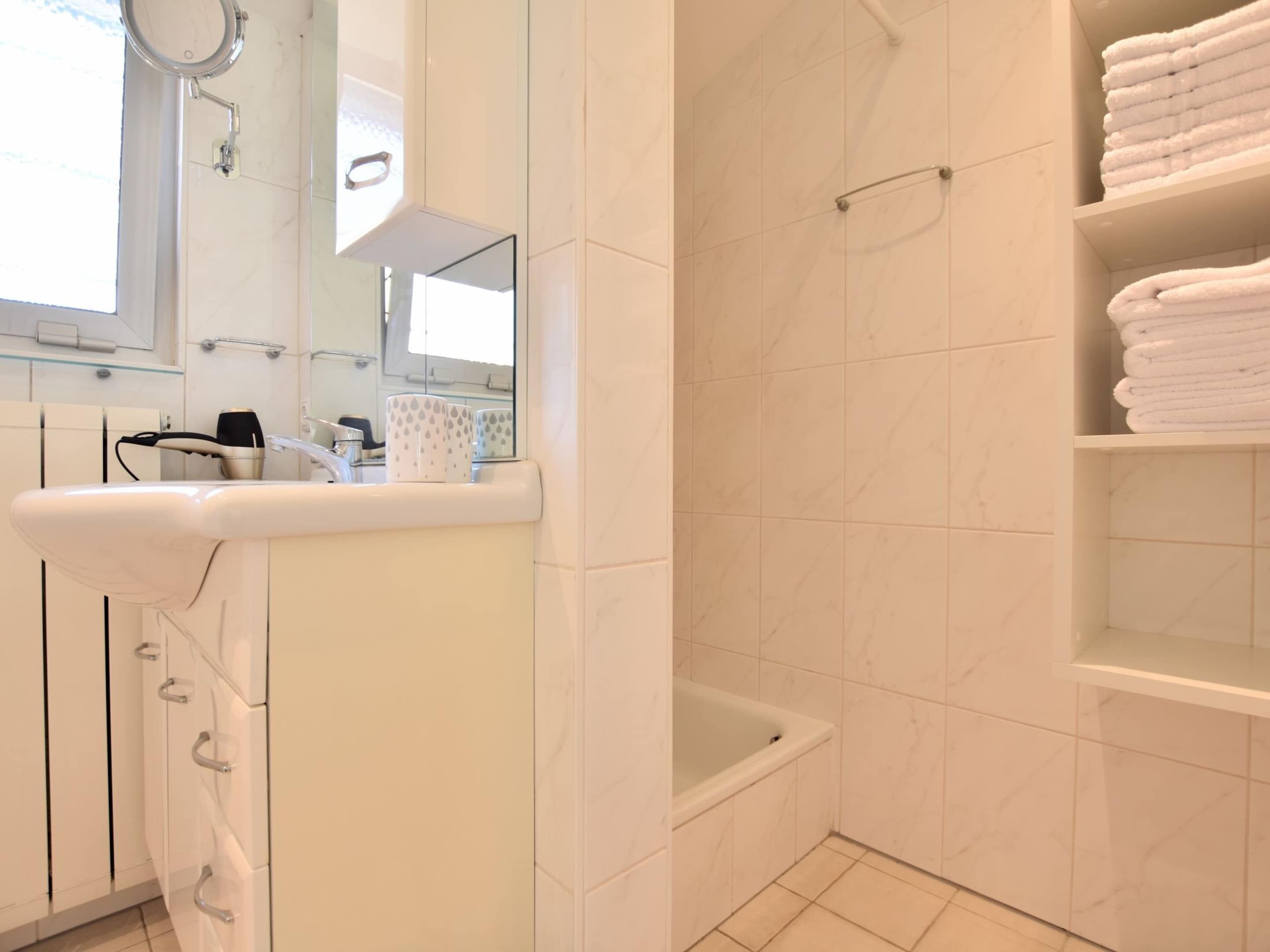 A modern bathroom with a white sink, mirror, and a bathtub.
