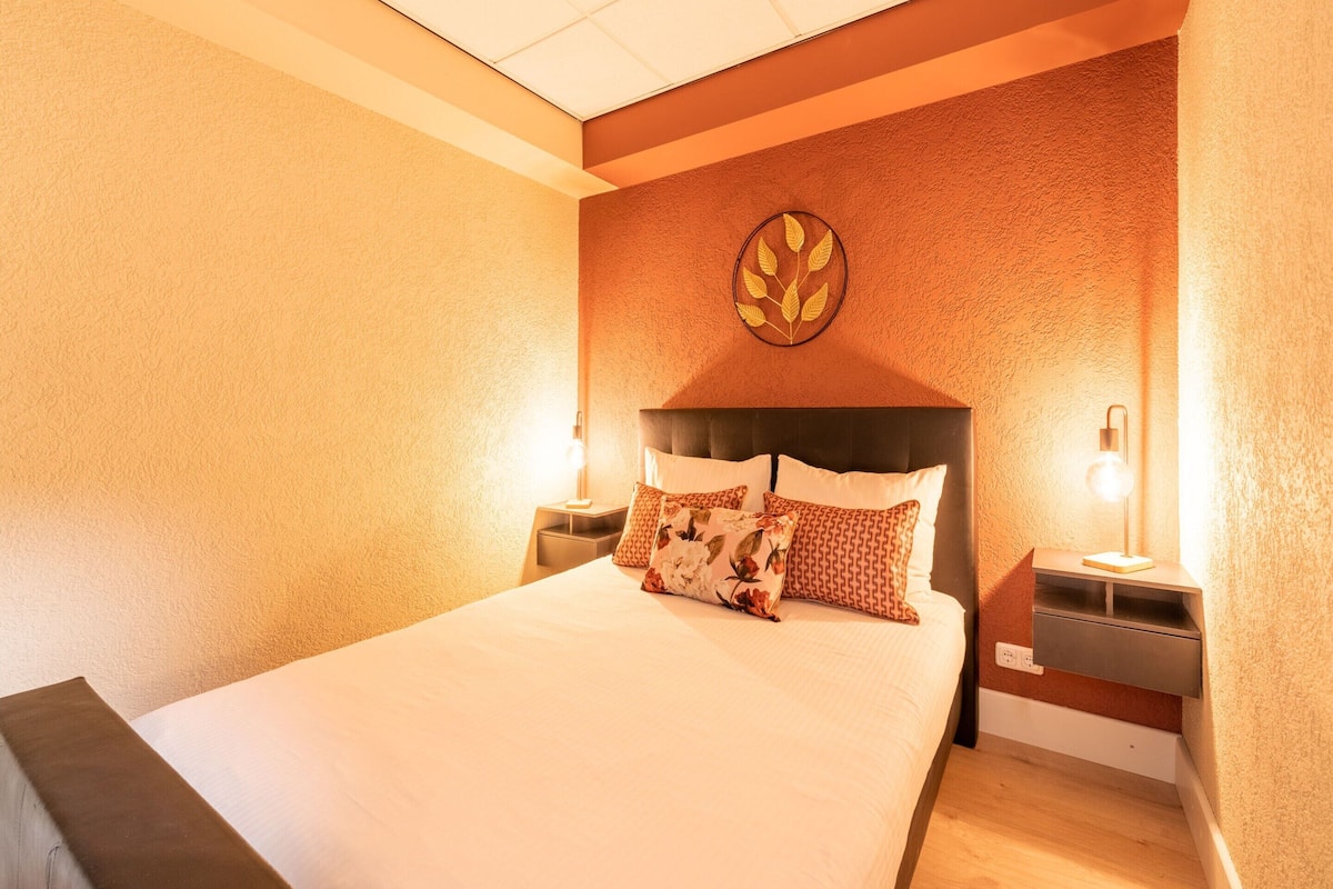Una habitación de hotel con una cama grande, dos mesitas de noche y una lámpara en el techo.