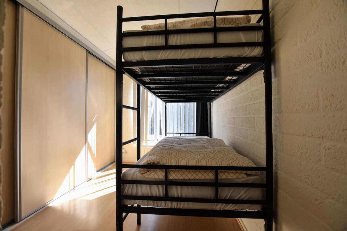 Una cama litera con una colcha estampada, una ventana con persianas y un piso de madera.