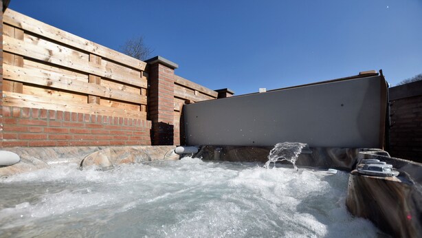 Ein Whirlpool mit Wasserstrahlen, umgeben von Holzwänden und einem Backsteinofen.