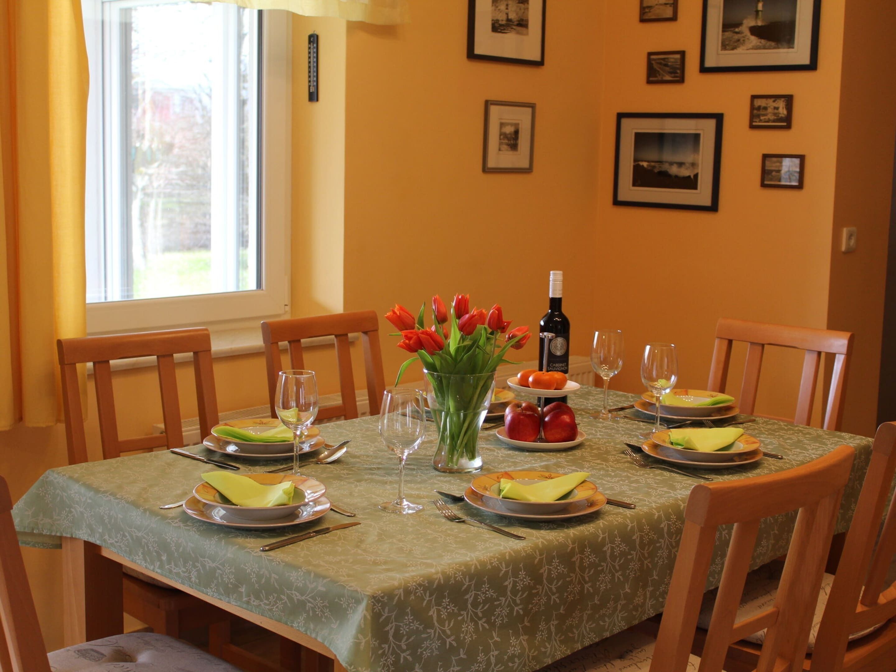 A dining table set with plates, glasses, and a bottle of wine, surrounded by chairs.
