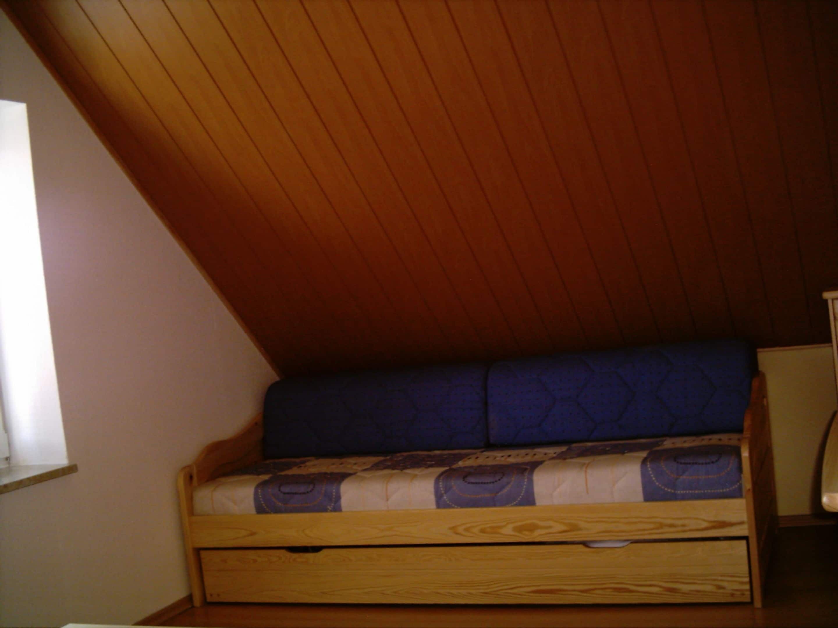 A small, wooden-framed bed with a blue mattress in a room with sloped wooden ceilings.