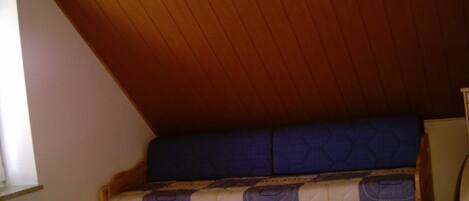 A small, wooden-framed bed with a blue mattress in a room with sloped wooden ceilings.