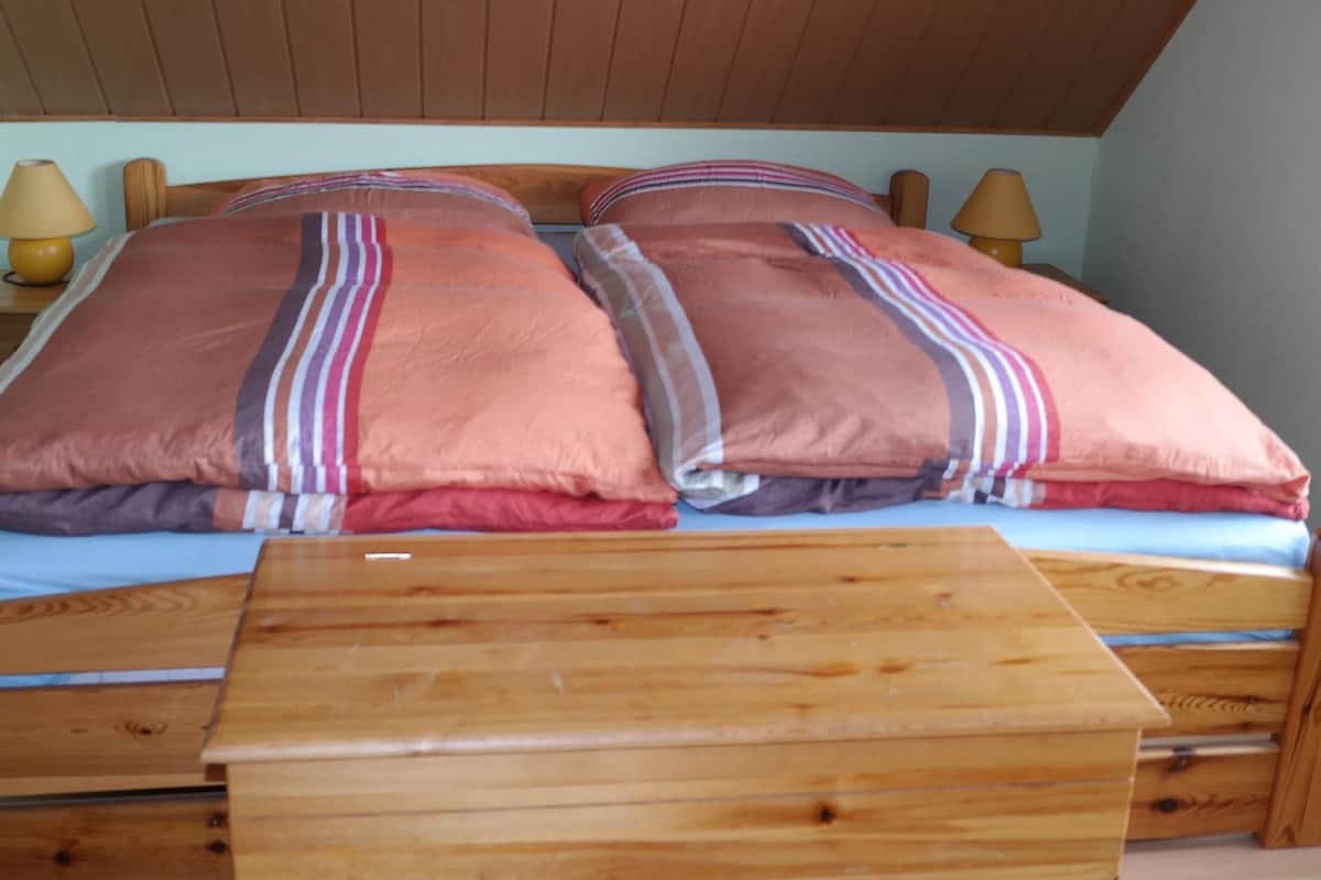 A wooden bed with two pillows and a wooden nightstand in a room with wooden ceiling and walls.