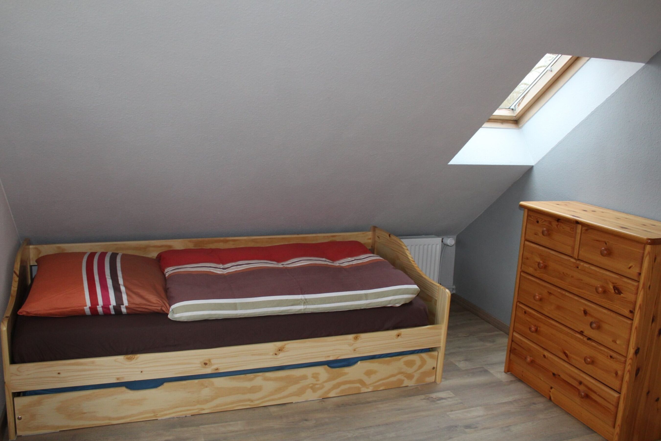 A small, single-bed room with a sloped ceiling and a skylight.