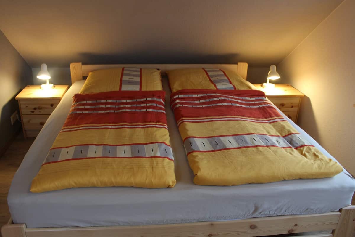 A double bed with a striped blanket, two bedside tables with lamps, and a wooden headboard.