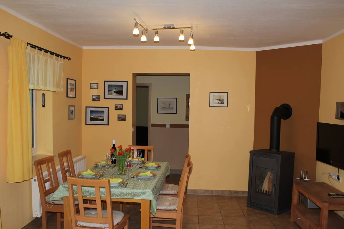 A dining area with a table set for four, a wood-burning stove, and framed pictures on the walls.