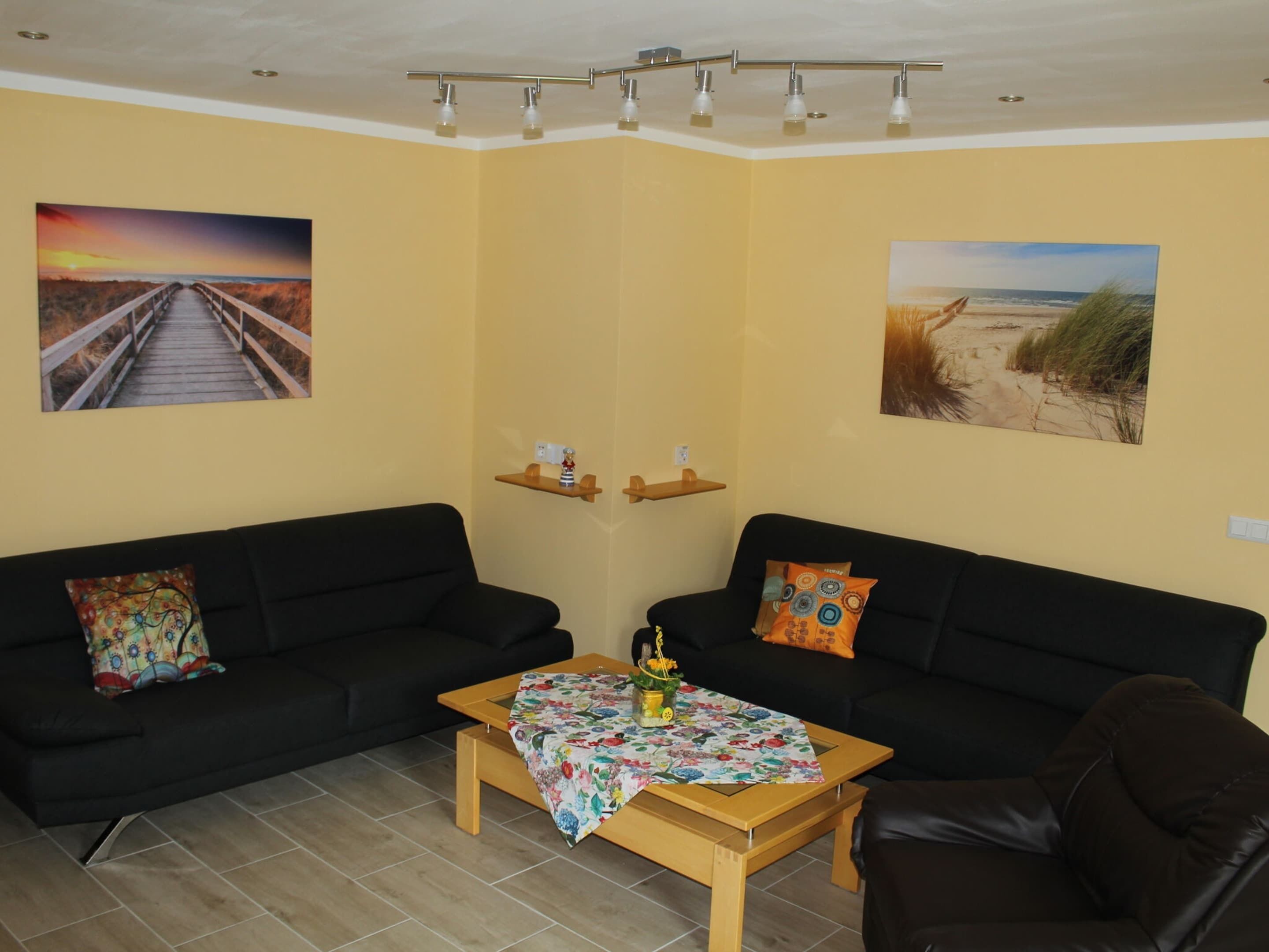 A living room with two black sofas, a wooden coffee table, and two wall-mounted shelves with decorative items.