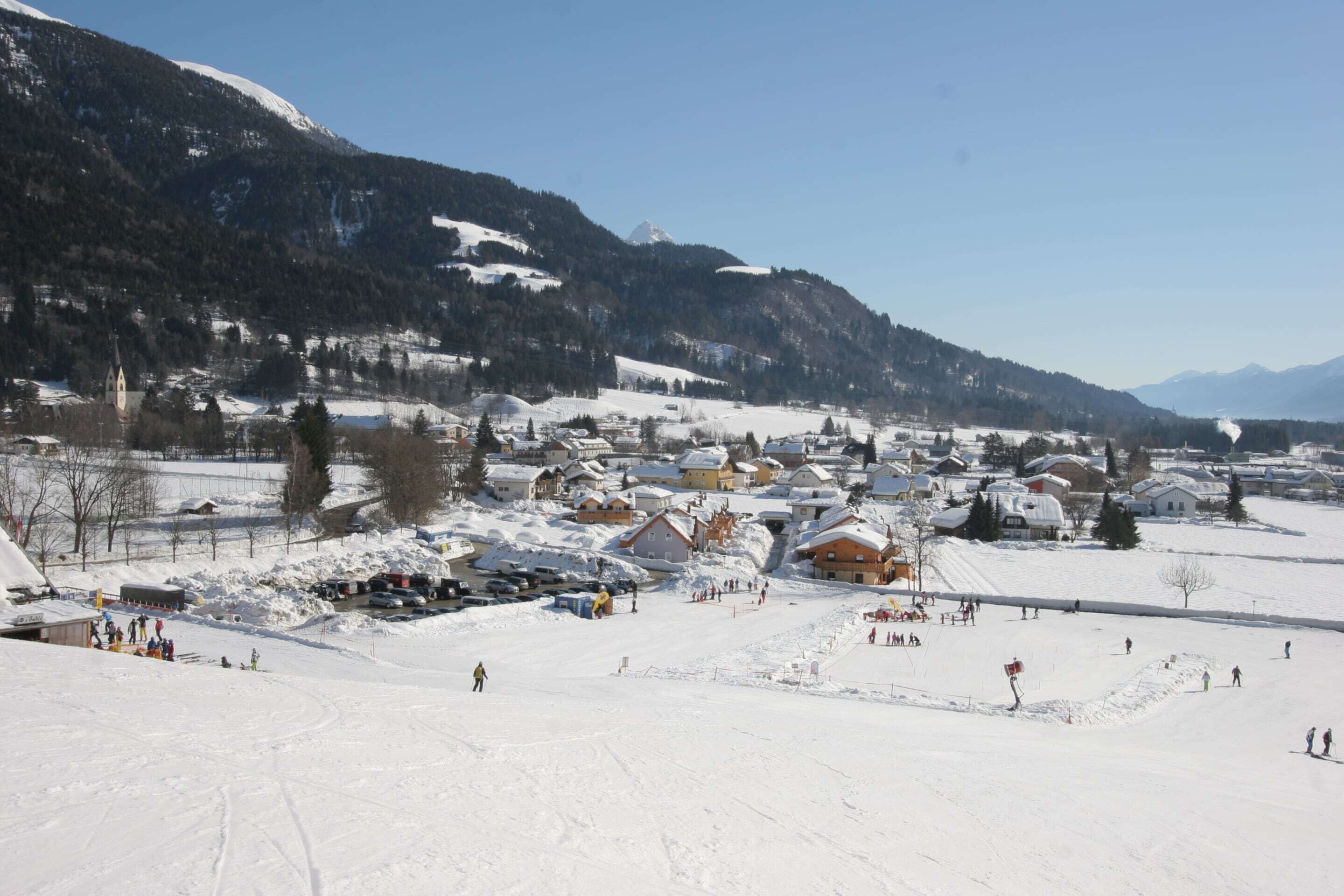 A snow-covered village with buildings and a church, surrounded by mountains.