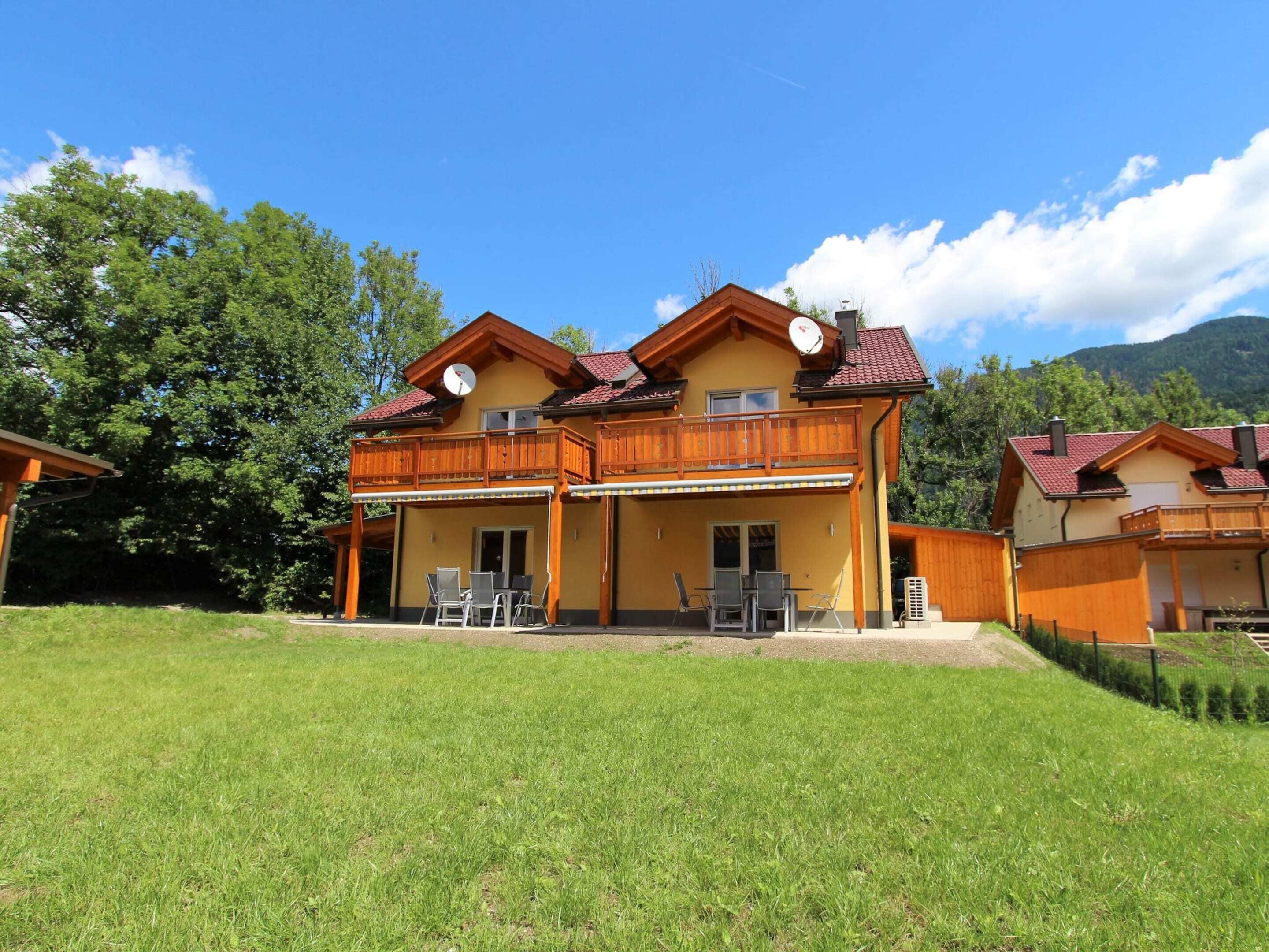 Une maison à deux étages avec un balcon, une terrasse couverte et une pelouse devant.