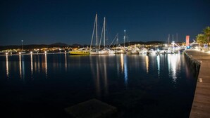 A marina at night with several boats docked, a wooden walkway, and a distant cityscape. - Stylish one Bedroom Apartment Just a few Steps From the sea (Golfo Aranci)