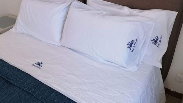 A neatly made bed with white linens and pillows, a brown headboard, and a visible power outlet on the wall. - Seafront Apartment in Villa With Swimming Pool and Parking (Alcamo)
