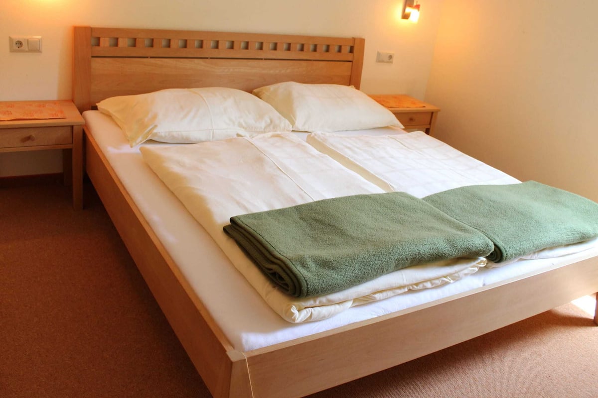 Ein ordentlich bezogenes Bett mit weißen Leinen und einem grünen Handtuch, ein Holz-Kopfteil, zwei Nachttische und Wandleuchten.