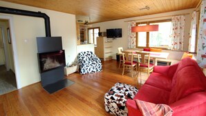A cozy living room with a fireplace, a red sofa, and a dining area with a table and chairs. - Sunlit Cabin With Jacuzzi in Turracherhohe (Stadl-Predlitz)