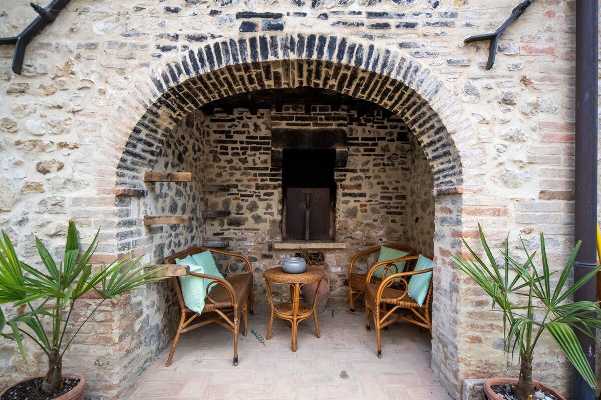 An outdoor seating area with wicker chairs and potted plants, a stone wall, and a brick fireplace.