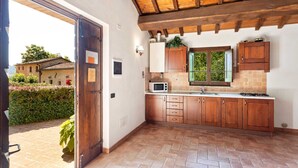 A kitchen with wooden cabinets, a microwave, and a window overlooking greenery.