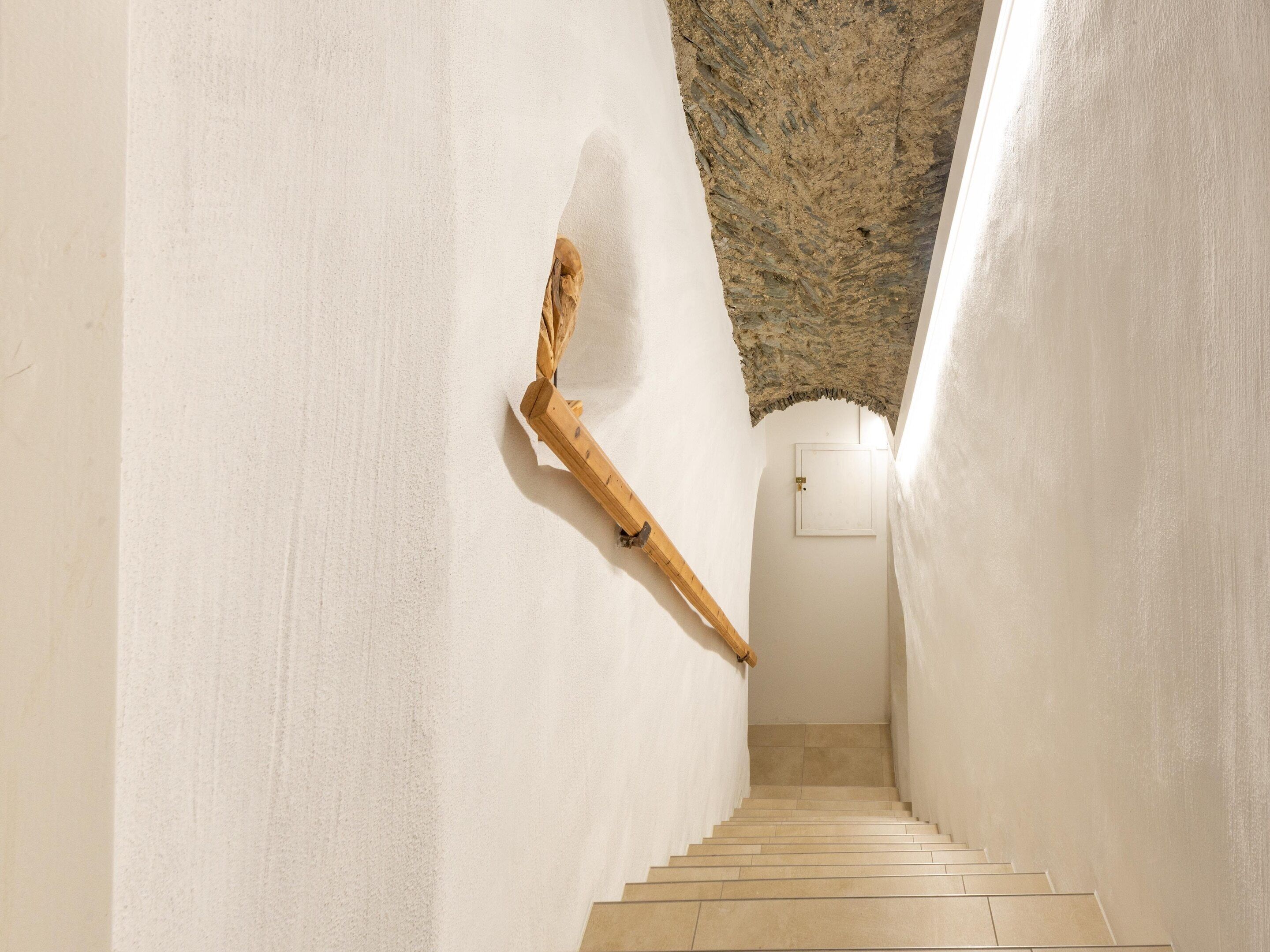 Eine schmale Treppe mit weißen Wänden und einem hölzernen Geländer.