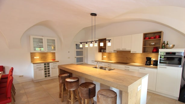 Una cocina moderna con una isla central, taburetes de bar, muebles blancos y un horno empotrado.