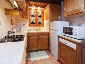 A compact kitchen with wooden cabinets, a white microwave, a stove, and a refrigerator. - Stylish Apartment in Sohl With Terrace (Bad Elster)