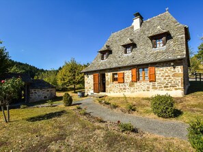 Ein Steinhaus mit geneigtem Dach, Holzläden und einem Kiesweg zum Eingang.