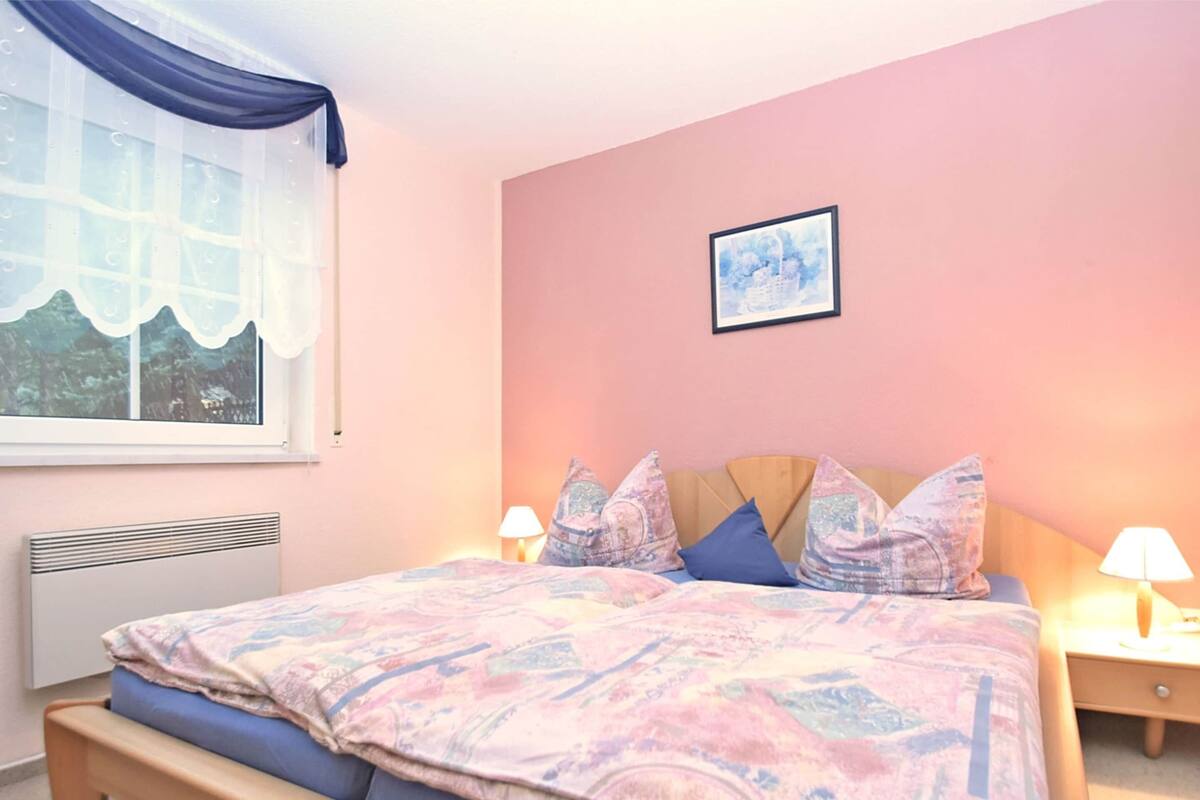 Ein Schlafzimmer mit Bett, Fenster mit Blick, einem Wandbild und Nachttischlampen.