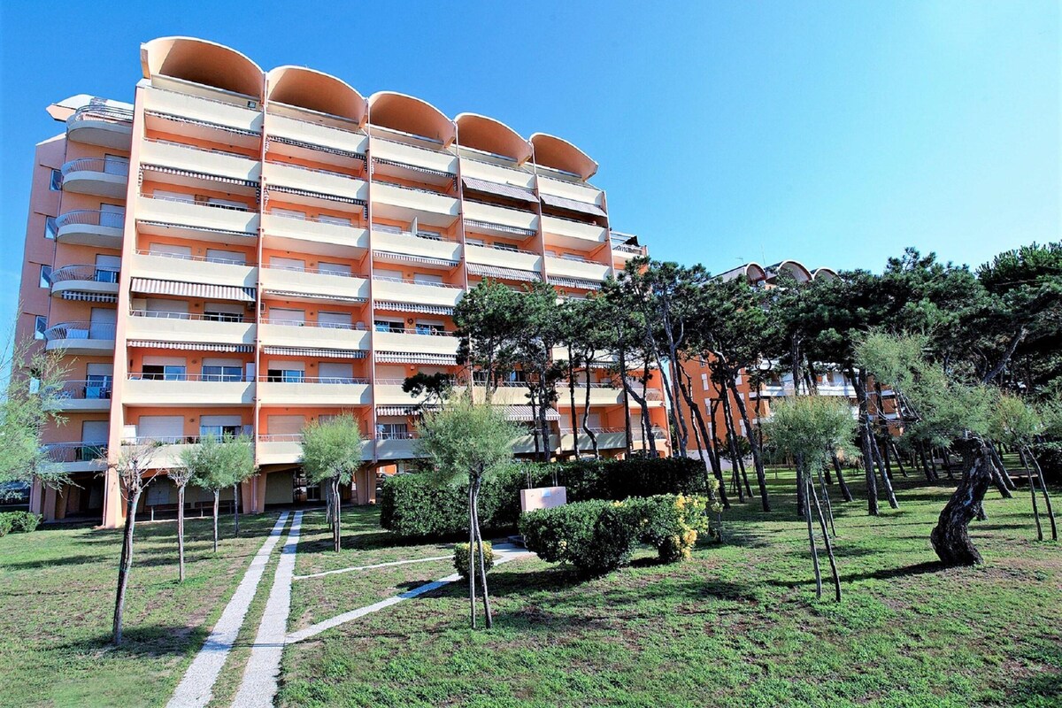 A multi-story hotel with balconies, a garden area with trees, and a clear sky.
