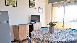 A room with a patterned tablecloth, a television on a stand, a refrigerator, and a potted plant. - Nice Apartment in Porto Santa Margherita With Terrace (Caorle)