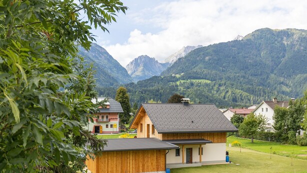 Een bergdorp met traditionele houten huizen, een klein hotel en uitgestrekte groene velden.