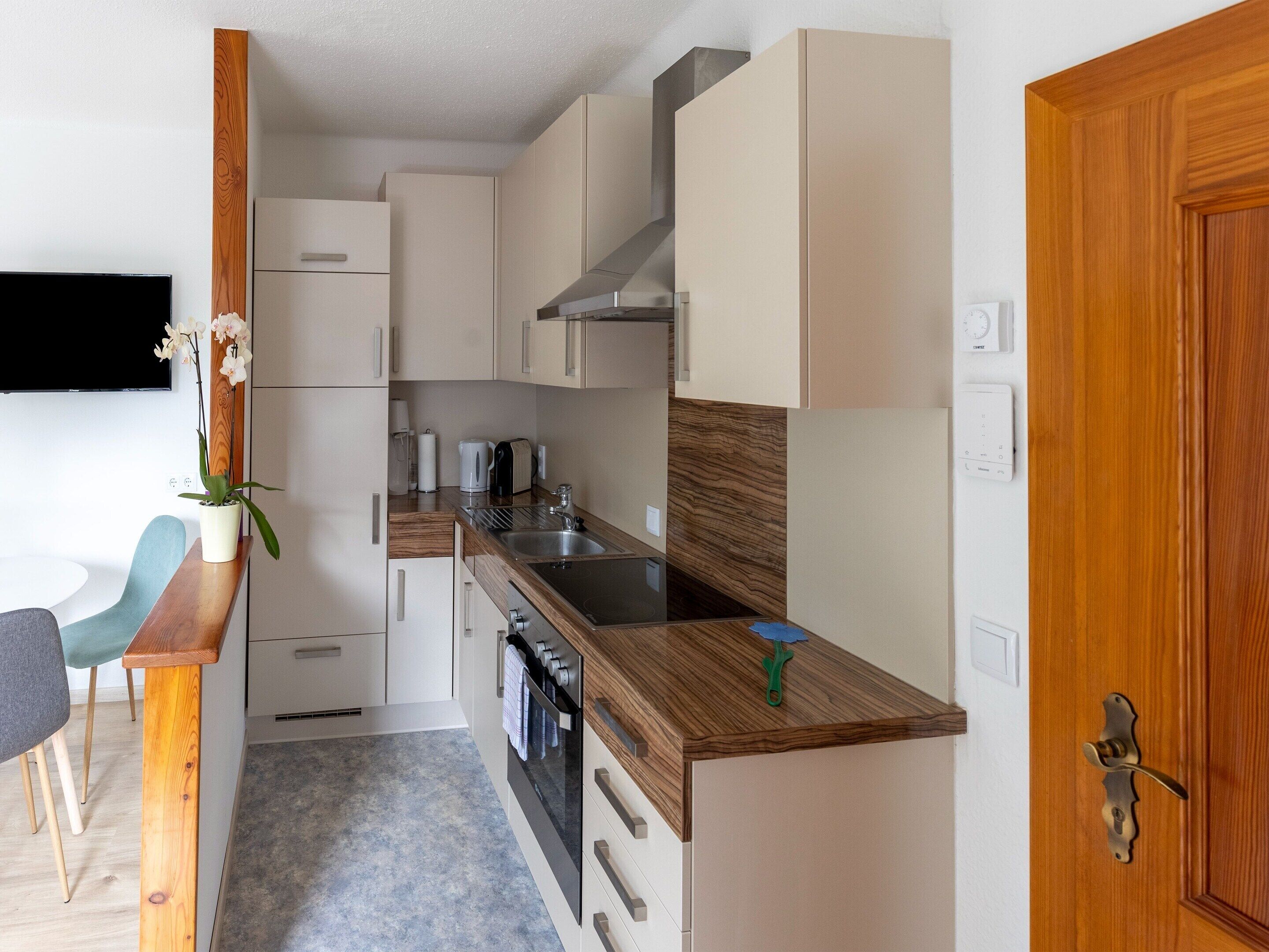 A compact kitchen with a wooden countertop, stainless steel sink, and white cabinetry. There is a small dining area with a chair and a table.